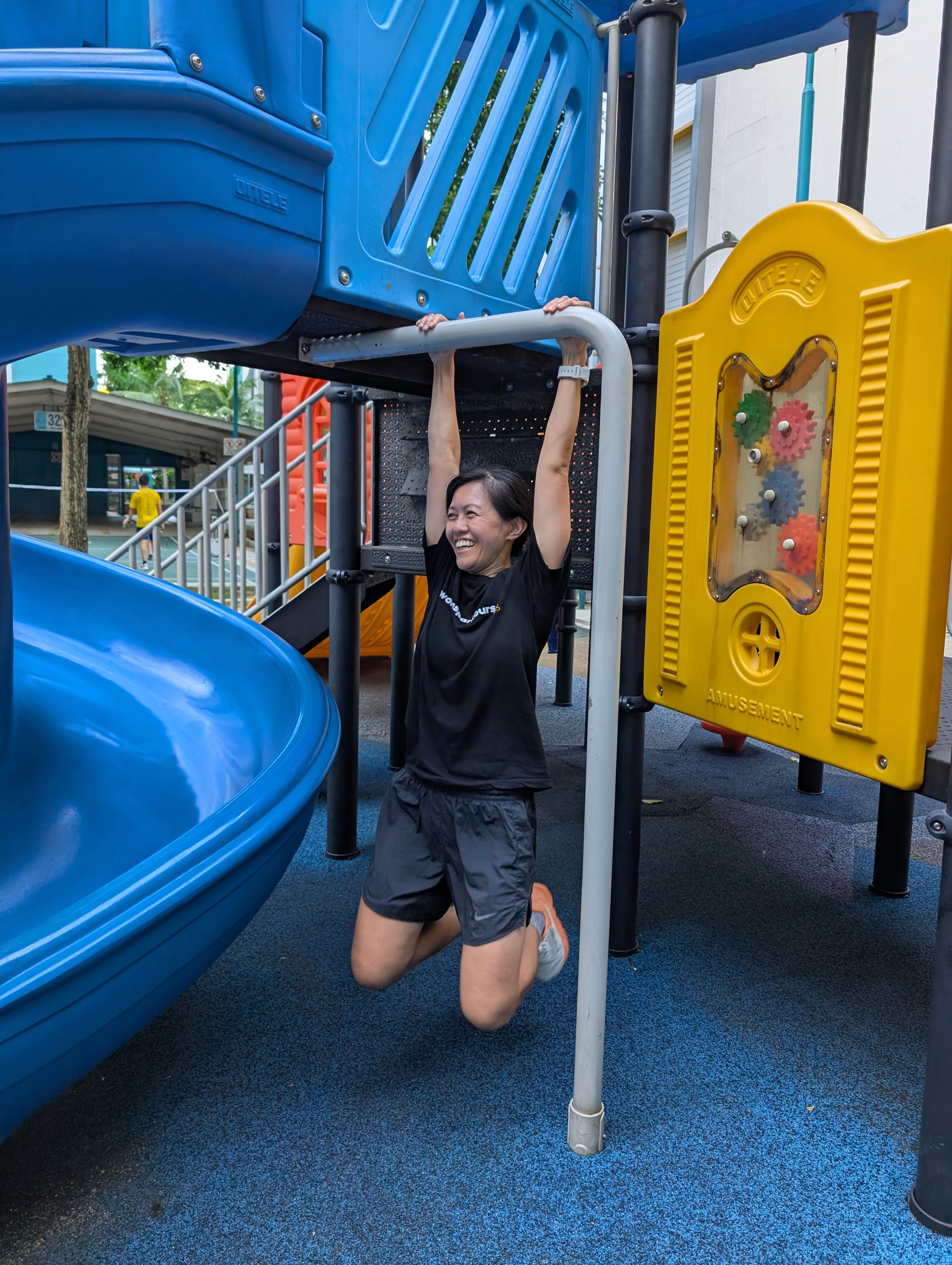 Liza laughing mid-swing on playground monkey bars during an outdoor workout